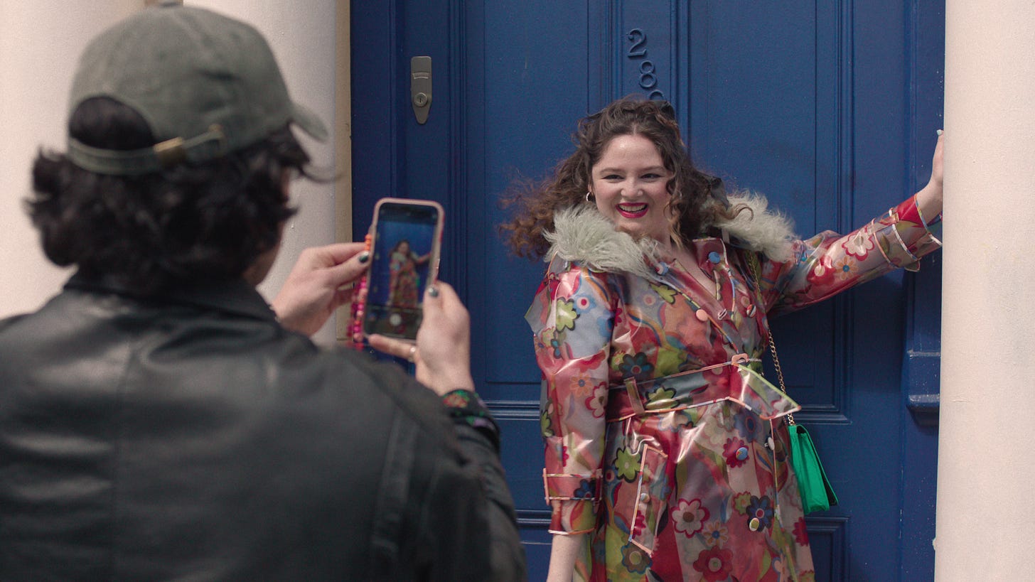 Jess from Too Much wears a patterned jacket in front of a blue door