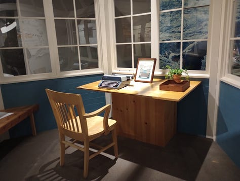 Desk with wooden chair and typewriter in mock office; Annette typing;corner of typewriter with Annette's typed note