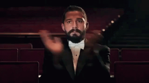 a man in a tuxedo and bow tie is sitting in an auditorium and clapping his hands .