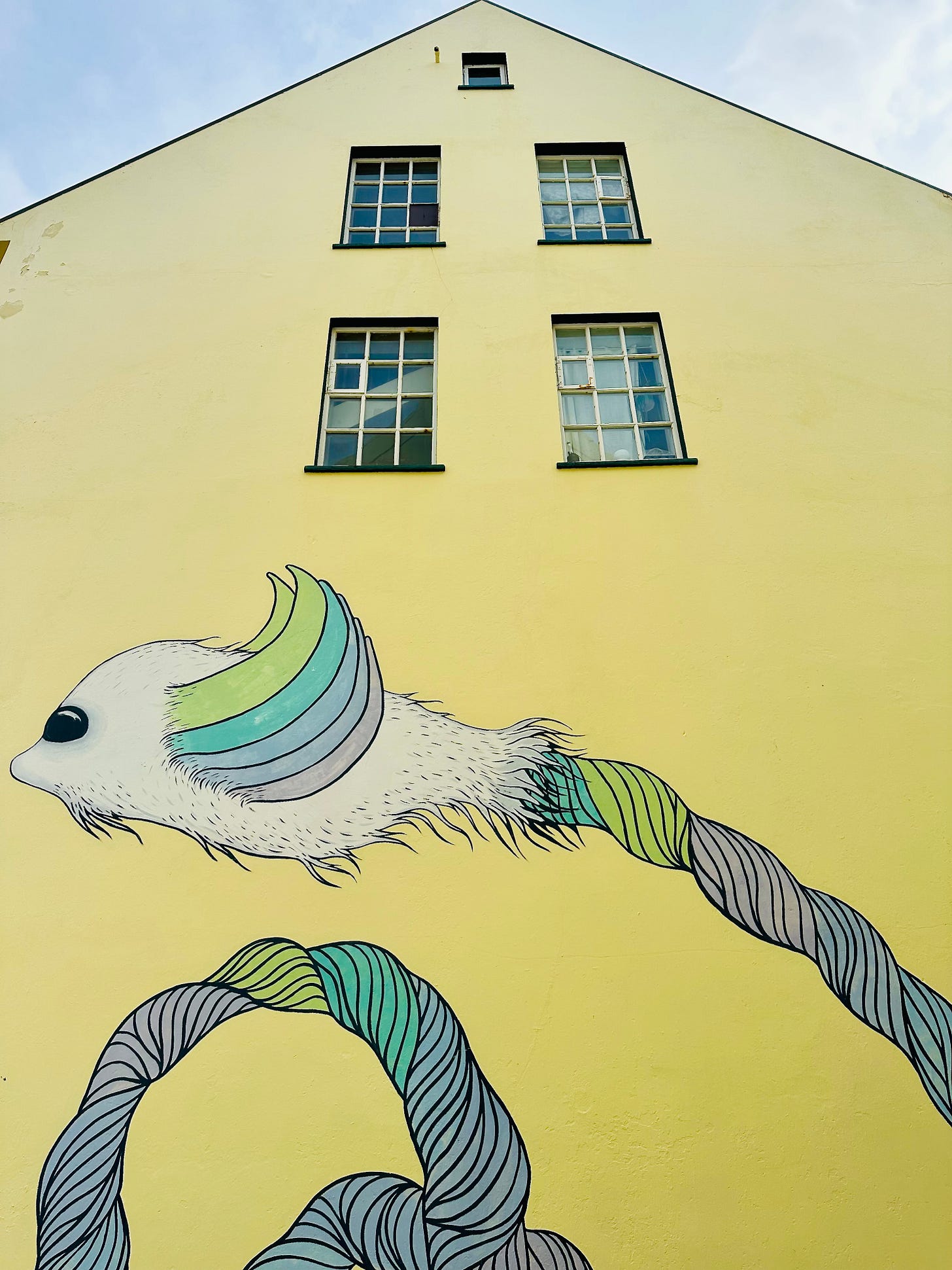 A lemon yellow home in Reykjavik, Iceland with a fanciful bird in flight painted on the side.