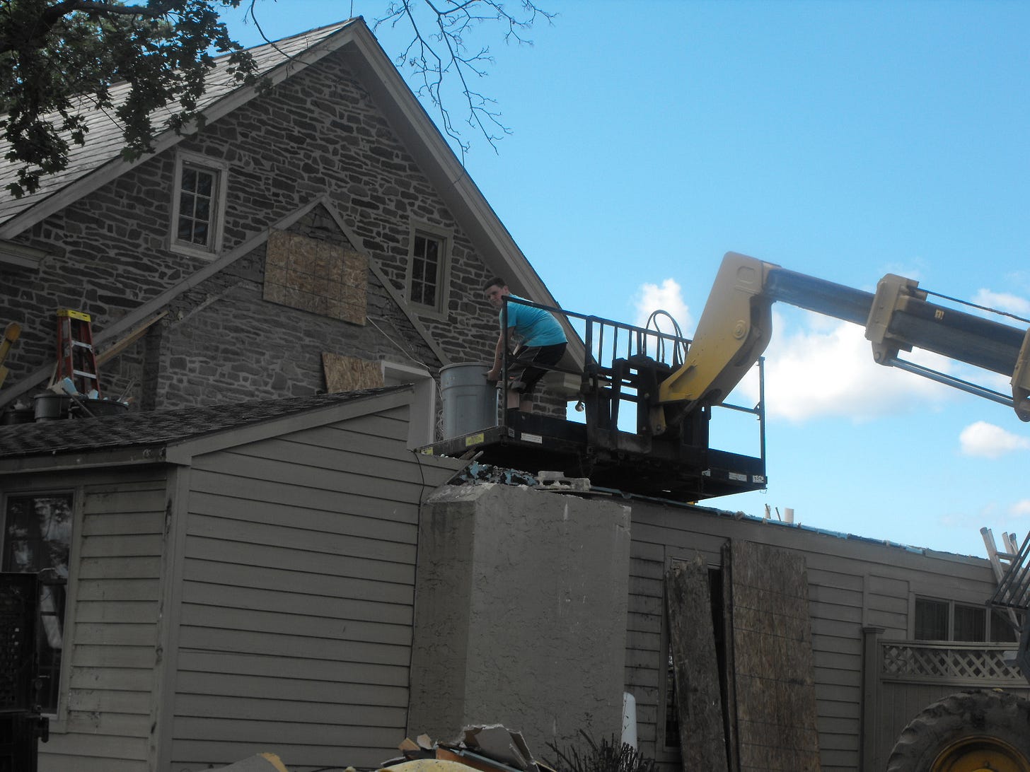Construction worker on a lift delivers materials to an old farmhouse undergoing renovations