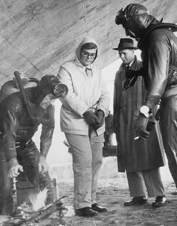 Eighteen-year-old Lowell Lee Andrews (center) stands as police search the Kansas River for parts of the guns he used to kill his family, 1958. Despite being described as the 'nicest boy in Wolcott,' Andrews was a Kansas University sophomore accused of murder.