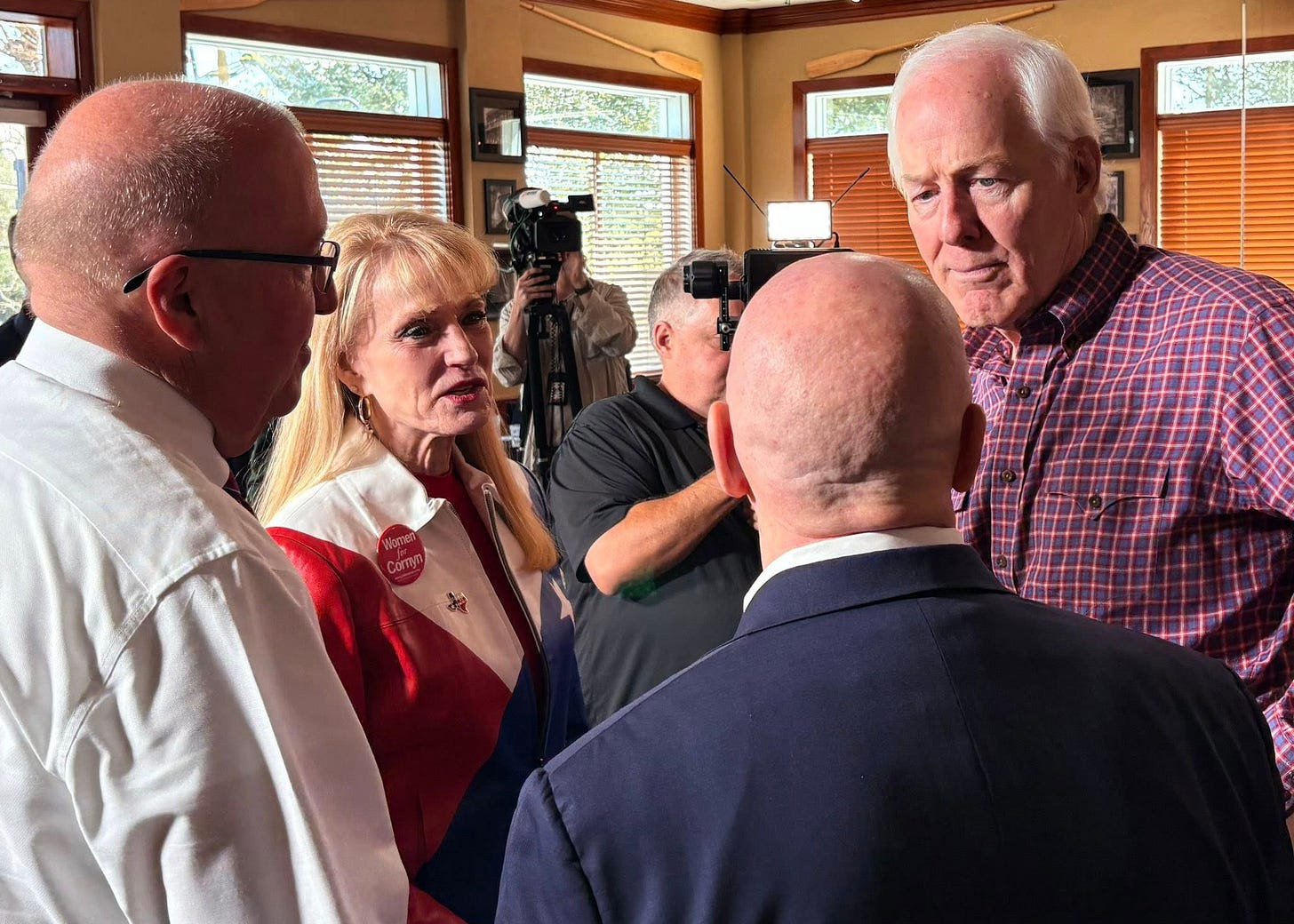 Photo of Texas Sen. John Cornyn (R) in a checked shirt, at right, speaking with supporters.