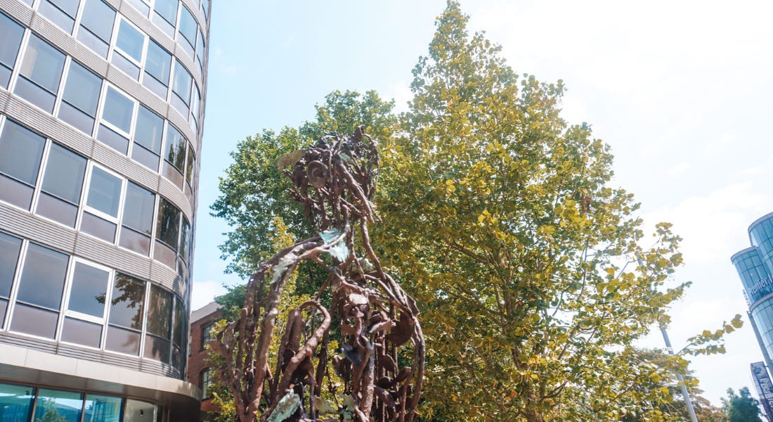 A bronze statue of Maid Marian with a tree and building behind it A bronze statue of Maid Marian with a tree and building behind it