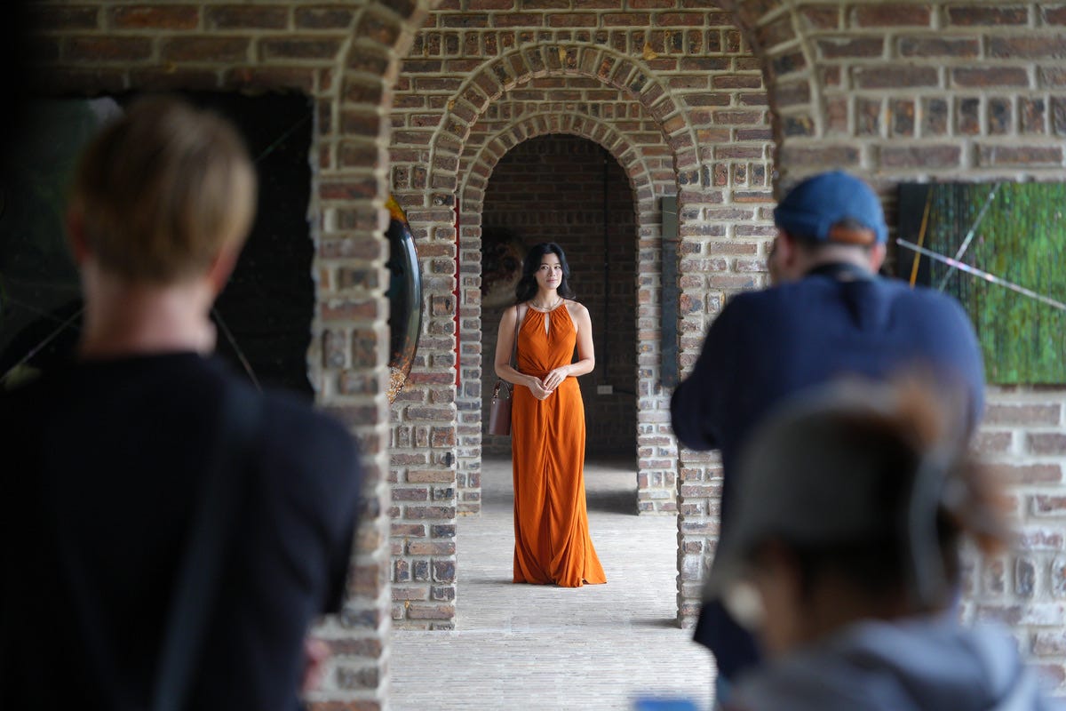 A model in an orange dress photographed by a stills and video crew in a brick archway