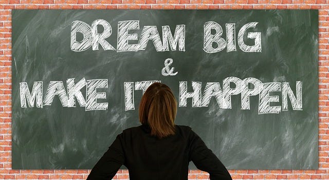 A digital drawing of a woman looking at a blackboard with the words "Dream Big & Make It Happen" written in large block letters