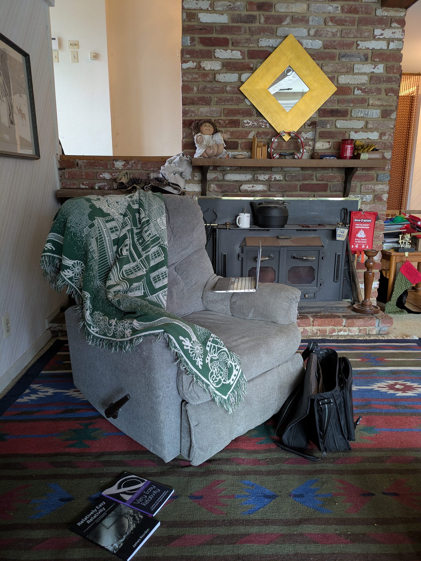 James Riordon’s writing space: a reclining chair with a laptop beside a wood stove in a brick-lined room. James Riordon’s writing space: a reclining chair with a laptop beside a wood stove in a brick-lined room.