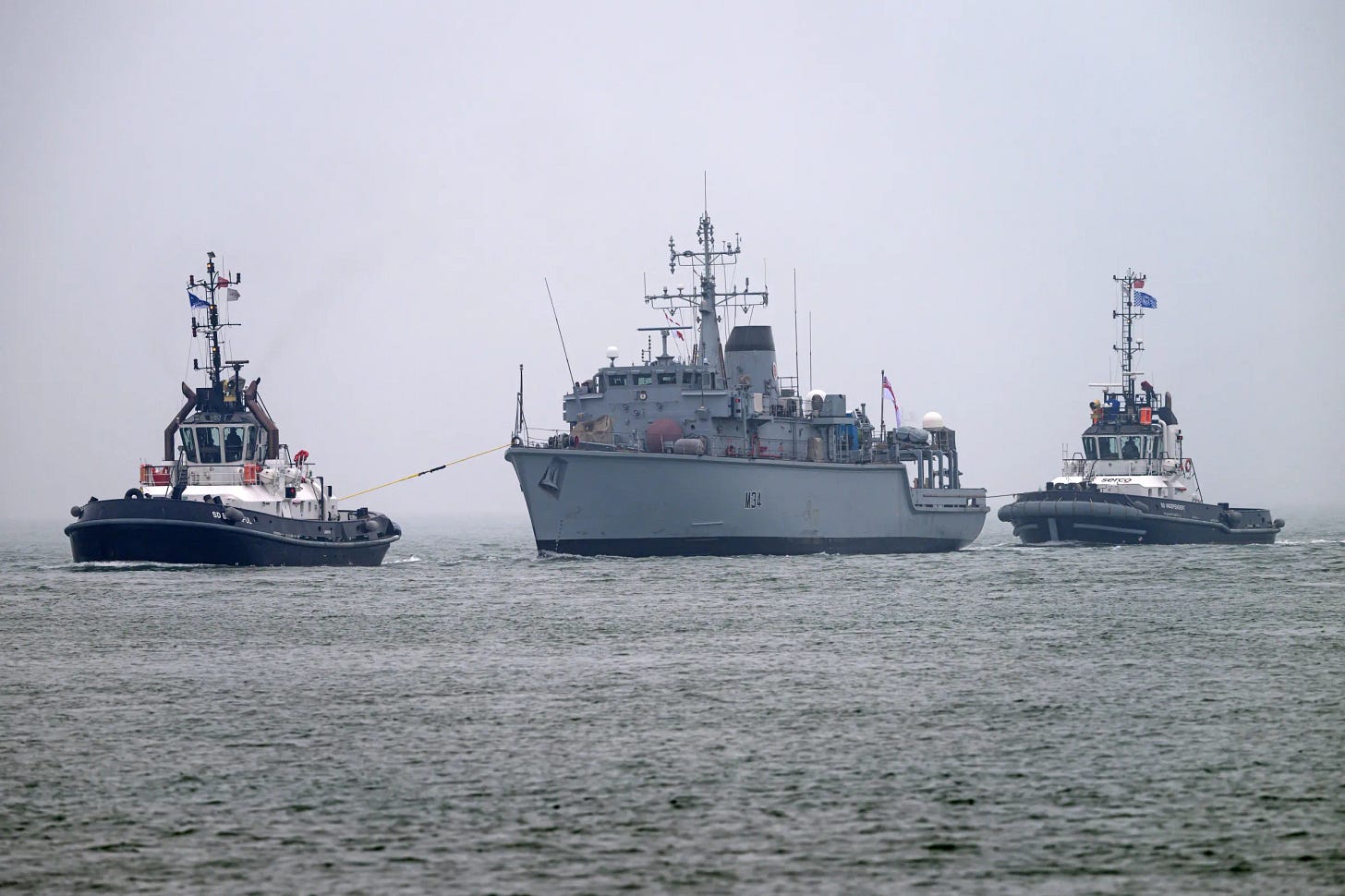 HMS Middleton (M34) mine warfare vessel being towed into Portsmouth by two tugboats.