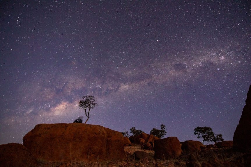 A band of stars in the sky behind a tree atop a rock in the outback. A band of stars in the sky behind a tree atop a rock in the outback.