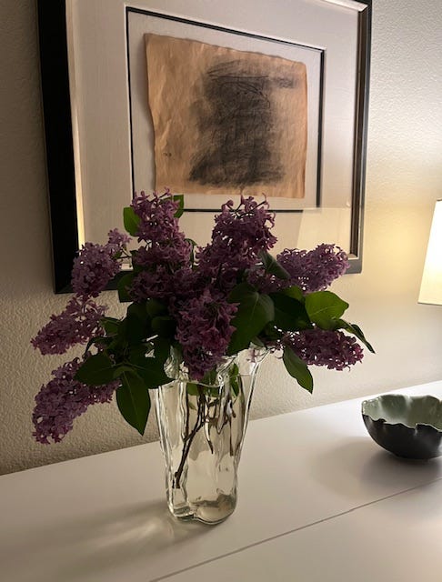 vase with purple lilacs on a hutch below artwork on the wall vase with purple lilacs on a hutch below artwork on the wall