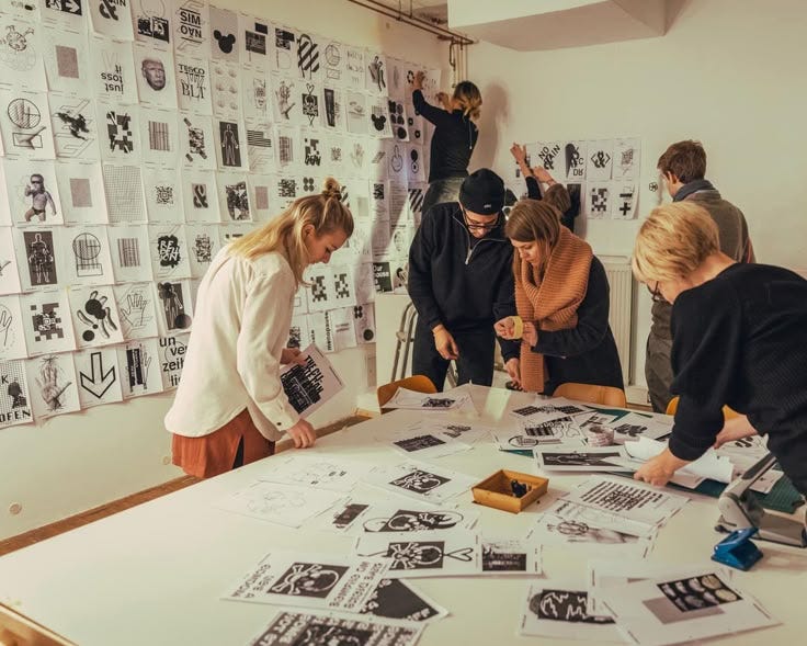 This may contain: several people standing around a table covered in black and white pictures, with one person pointing at something on the table