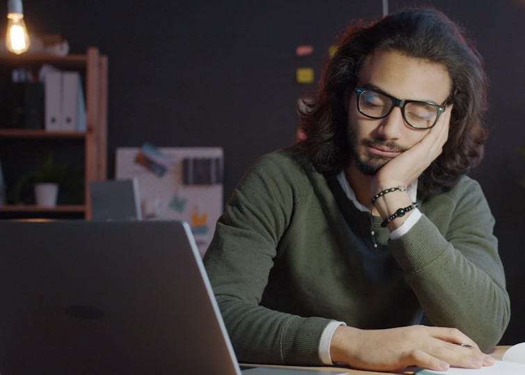 Man sleeping at desk with laptop and notebook.