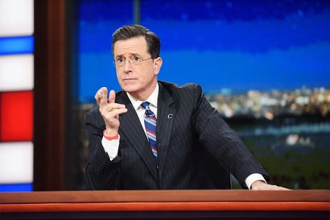Woman with brown hair wearing a black top with multicolored scarf; protesters and ICE agents; man with brown hair wearing a white dress shirt, ti, and black blazer; man with short black hair wearing a salmon-colored turtleneck and black blazer; man with gray hair wearing a white dress shirt, tie and black blazer.