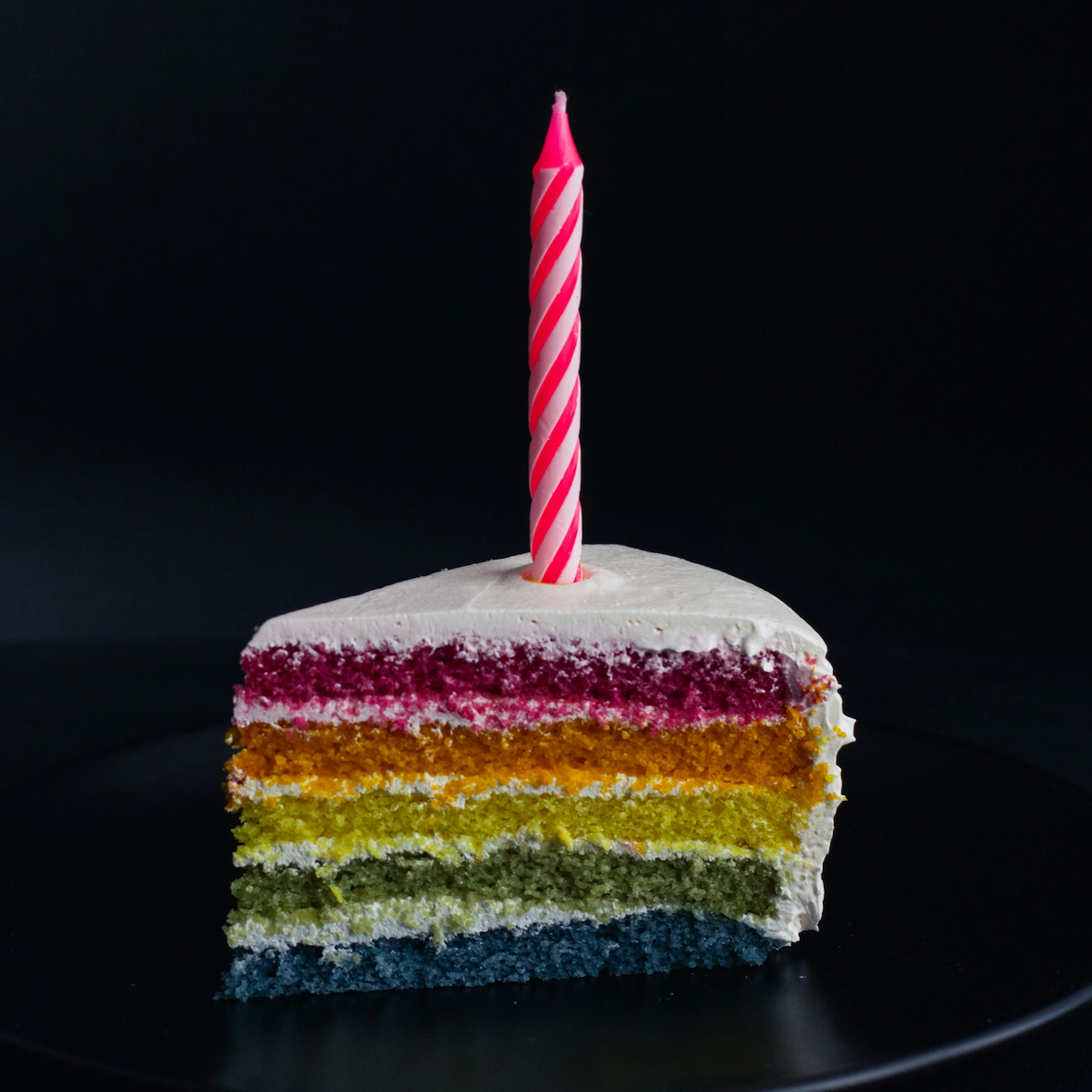 Birthday candle in a slice of rainbow cake
