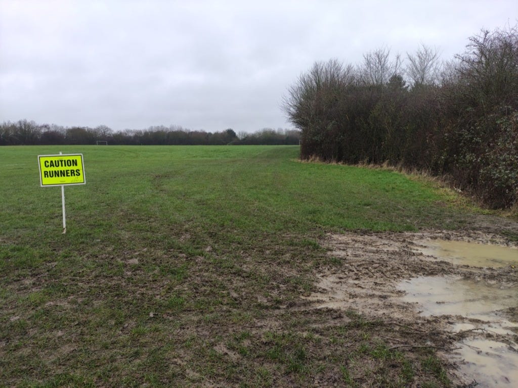 A caution runners sign in the field, with a muddy puddle off to one side.
