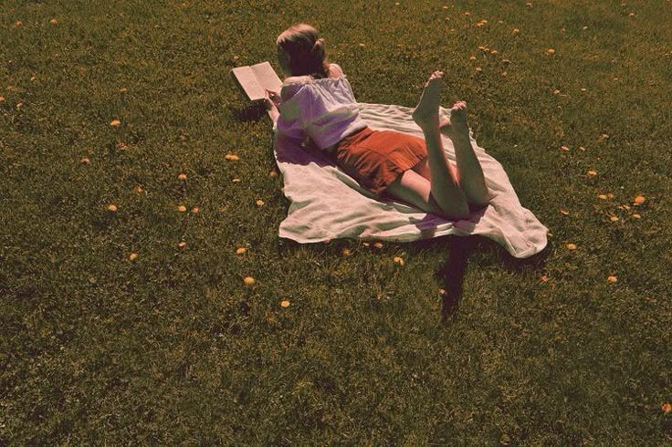 This may contain: a young boy laying on top of a blanket in the grass next to an umbrella