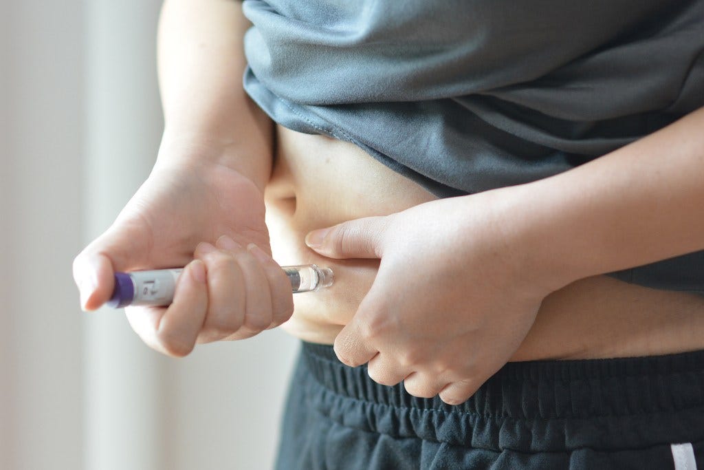 A person using an injection pen on their abdomen.