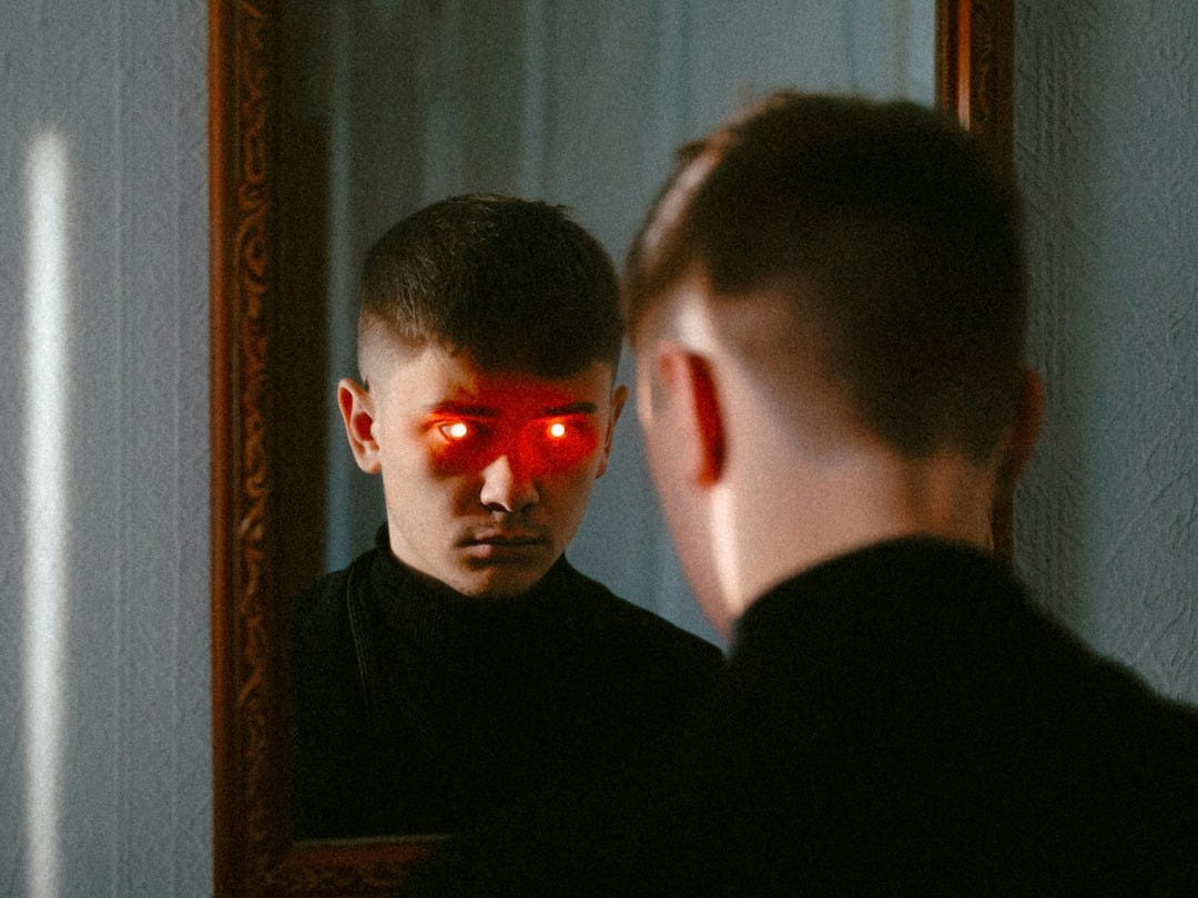 A man stares at his reflection with glowing eyes. A man stares at his reflection with glowing eyes.