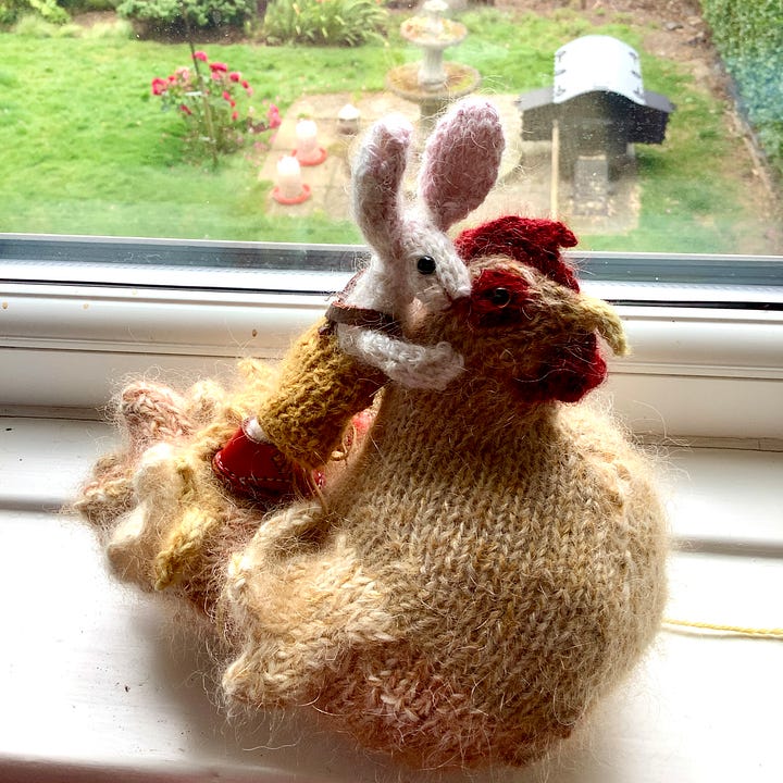 A knitted checking and a knitted rabbit become acquainted, the rabbit is sitting on the chicken and then the chicken is stood up.