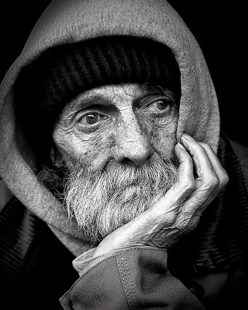 An old man sits with his chin resting on his palm as his elbow is on the table.