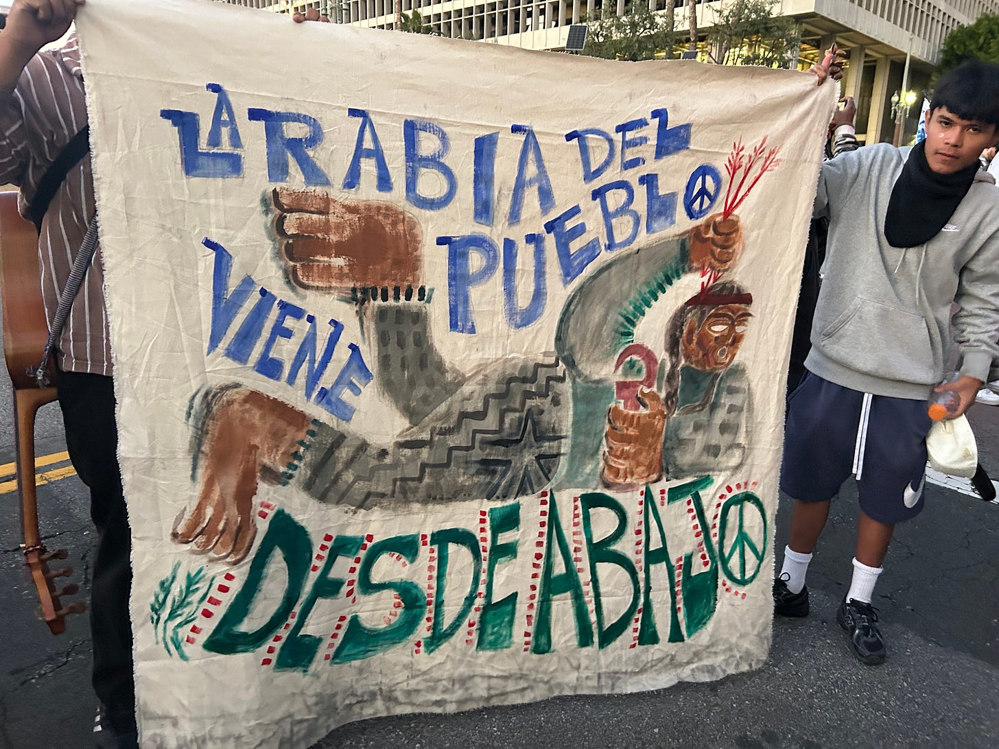 A young Brown Man Holds a Painted Banner that Reads in Spanish the Rage of the People Comes from Below A young Brown Man Holds a Painted Banner that Reads in Spanish the Rage of the People Comes from Below