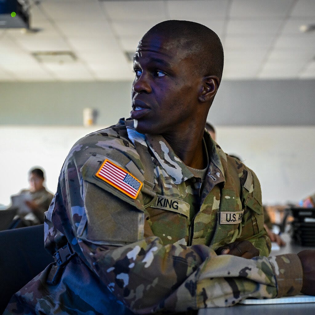 Joseph King, wearing a camouflage uniform, writing in a notebook in a classroom.