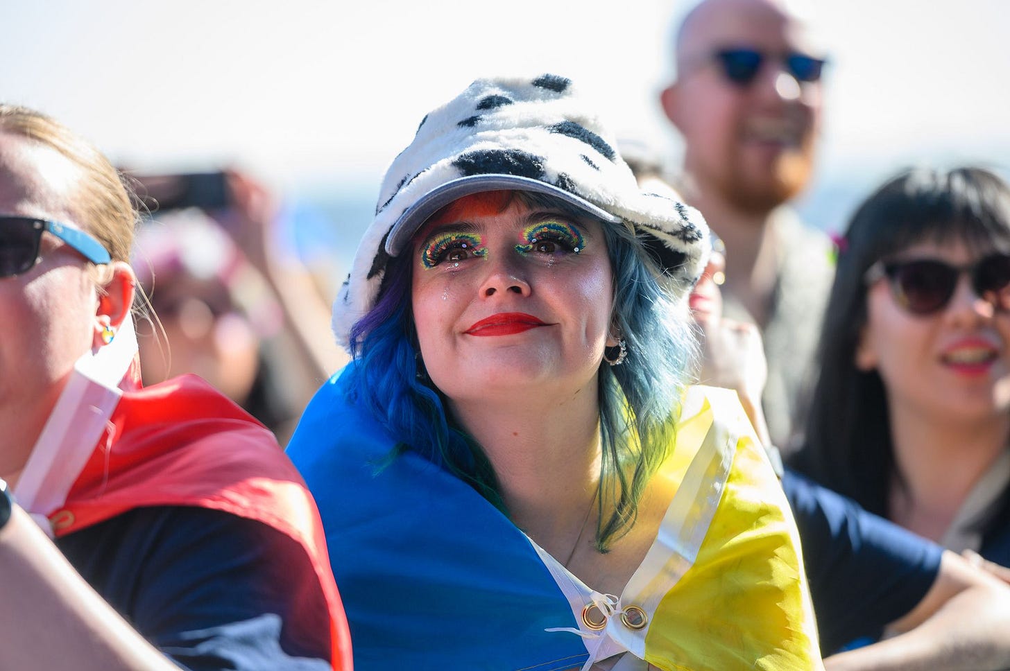 A woman in a Ukraine flag watches a live act on stage from the crowd.