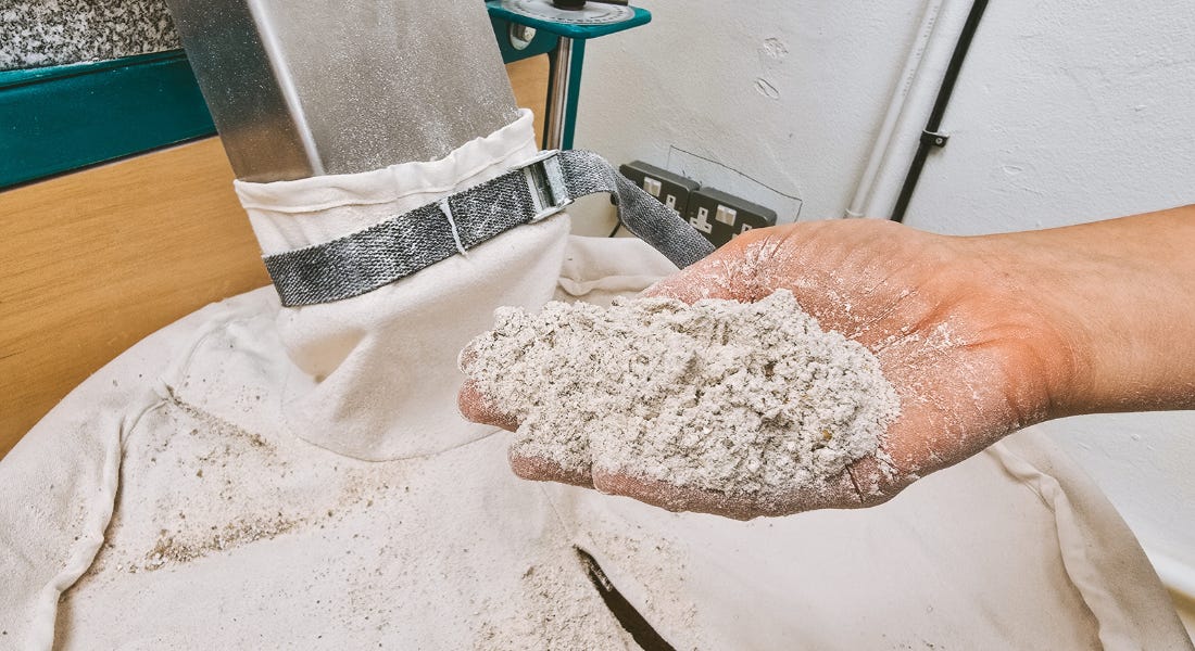 A hand holding a pile of flour in front of a milling machine