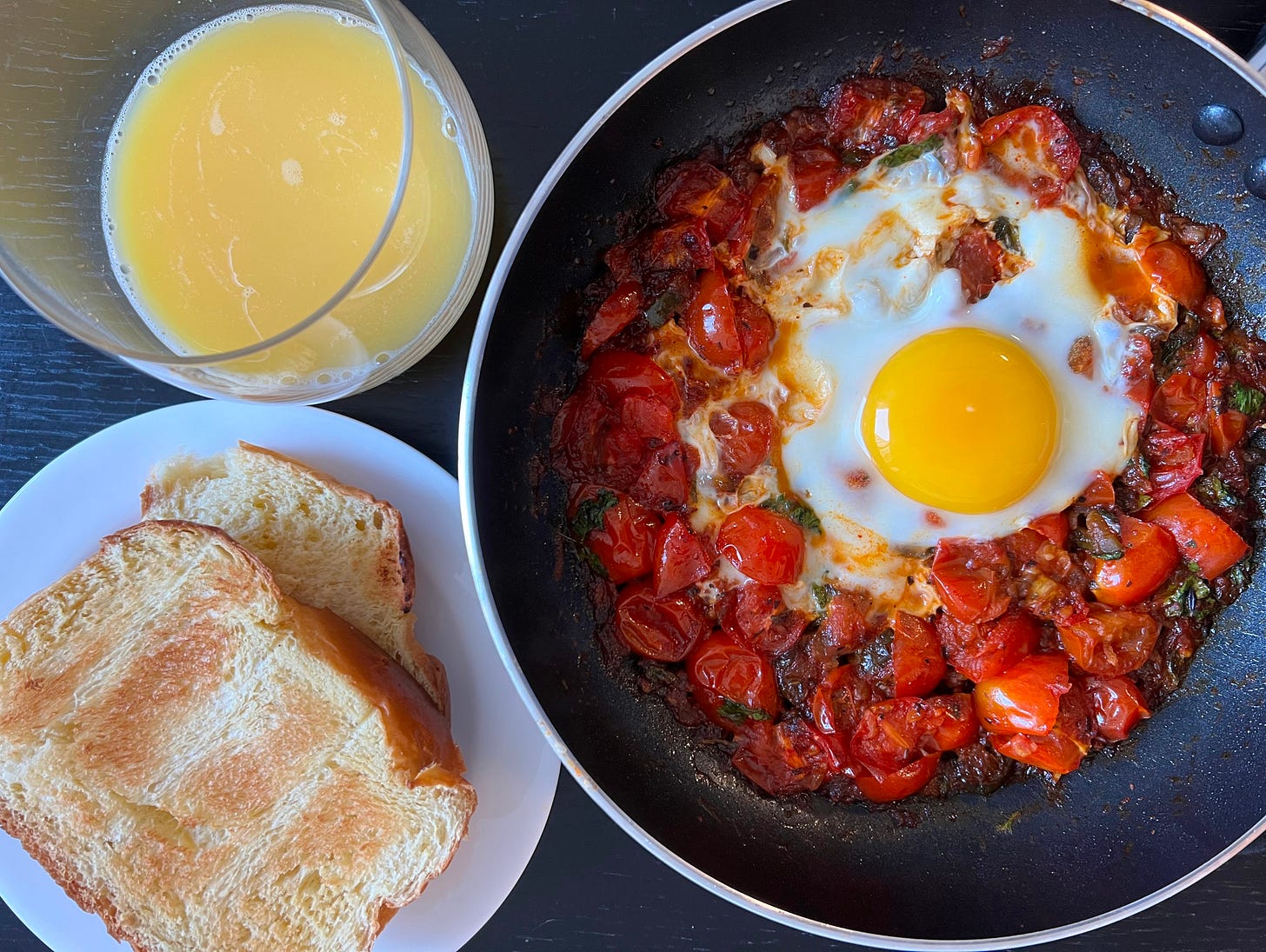 A skillet of classic shakshuka, showcasing tomatoes cooked into a rich, aromatic sauce with a perfectly poached egg. Served with two slices of brioche bread and a glass of orange juice, this dish epitomizes the simplicity and beauty of Mediterranean cooking. Prepared with love by Liat Portal, as part of her culinary storytelling of Foodie Disorder on The Liat Show.