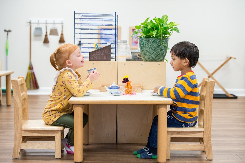 Two young children sharing tea together at a Montessori table during the Guidepost Montessori experience Two young children sharing tea together at a Montessori table during the Guidepost Montessori experience
