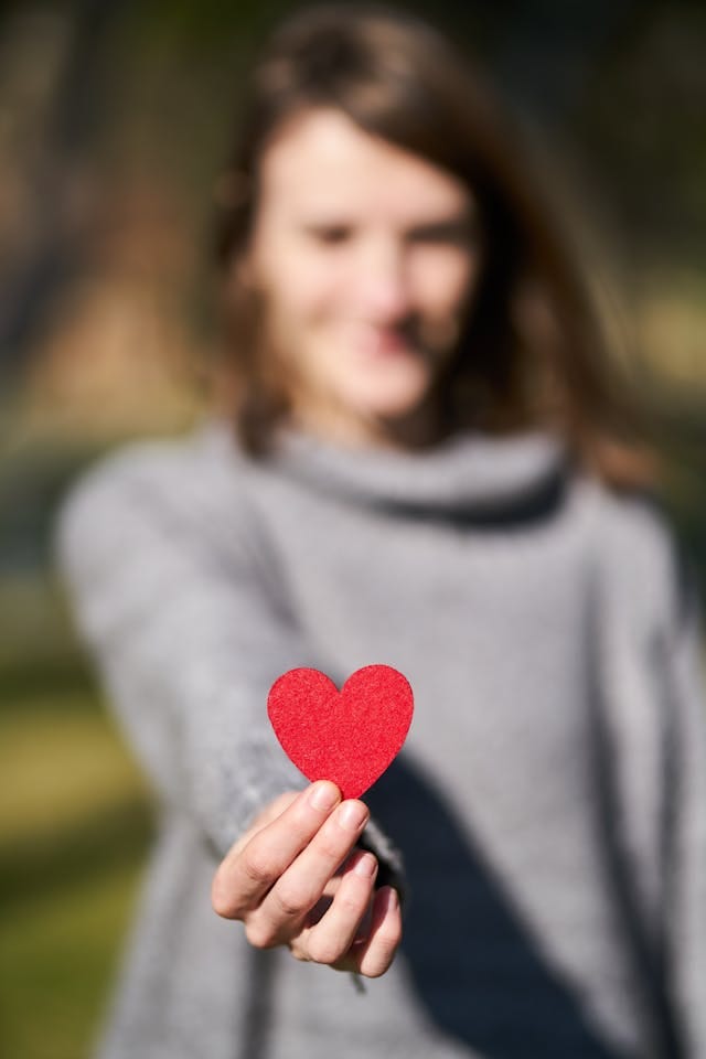Woman blurred into the background holding out a red cutout heart