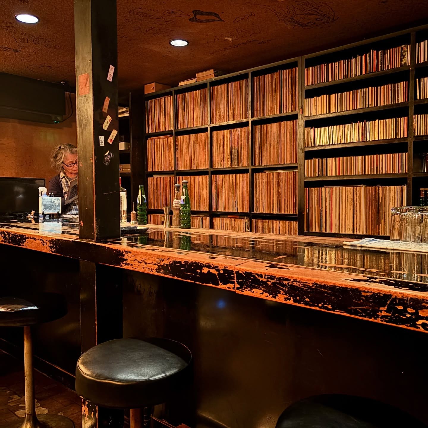A full wall of vinyl and CDs behind the wooden knackered bar of York, with the owner stage-left inspecting a record before playing it