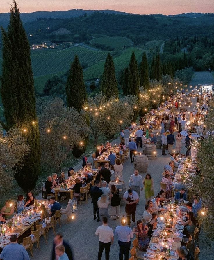 This may contain: a group of people sitting at tables in the middle of an outdoor dining area with candles on each table