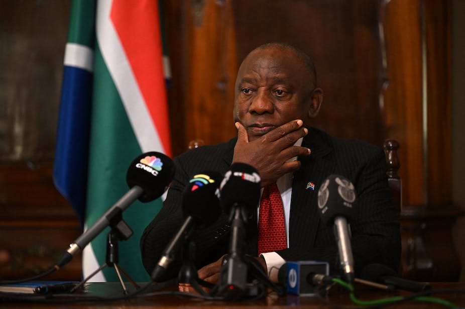 A man in a pensive mood, with his right hand to his chin, its in front of microphones.