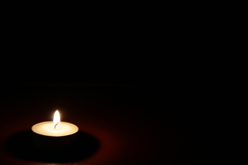 A small votive candle burning in the lower left corner of a large black frame