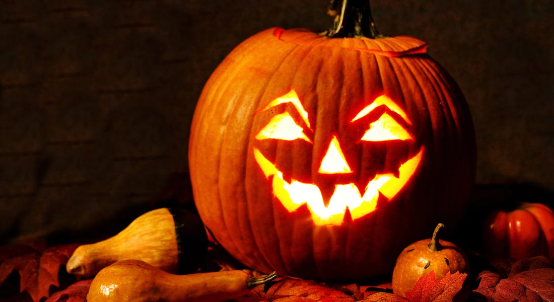 A pumpkin with a carved face with lights behind it on with other pumpkins surrounding it, in front of a black background