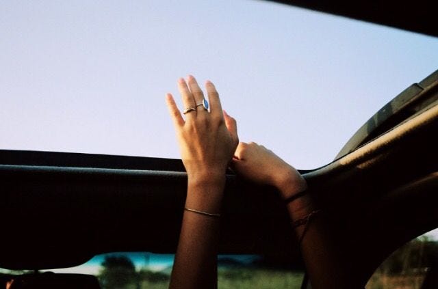 This may contain: two hands on the steering wheel of a car, while another person is holding their hand out