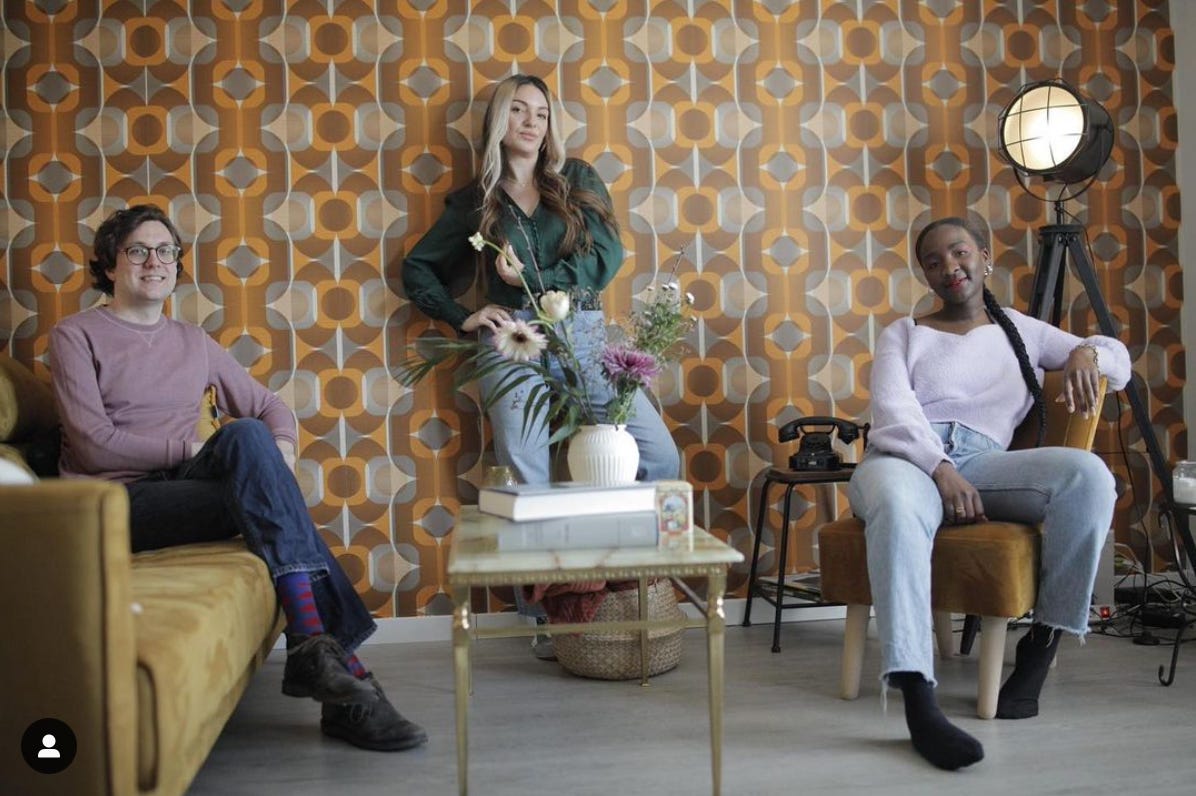 foto van de studio van fufu en dadels met daarin van links naar rechts: op de bank Sander Philipse in een oudroze rui, Suheyla Yalcin in groene blouse en Mungayende Helene Christelle in witte blouse. Het behang is typisch jaren ’70 bruin met oranje.