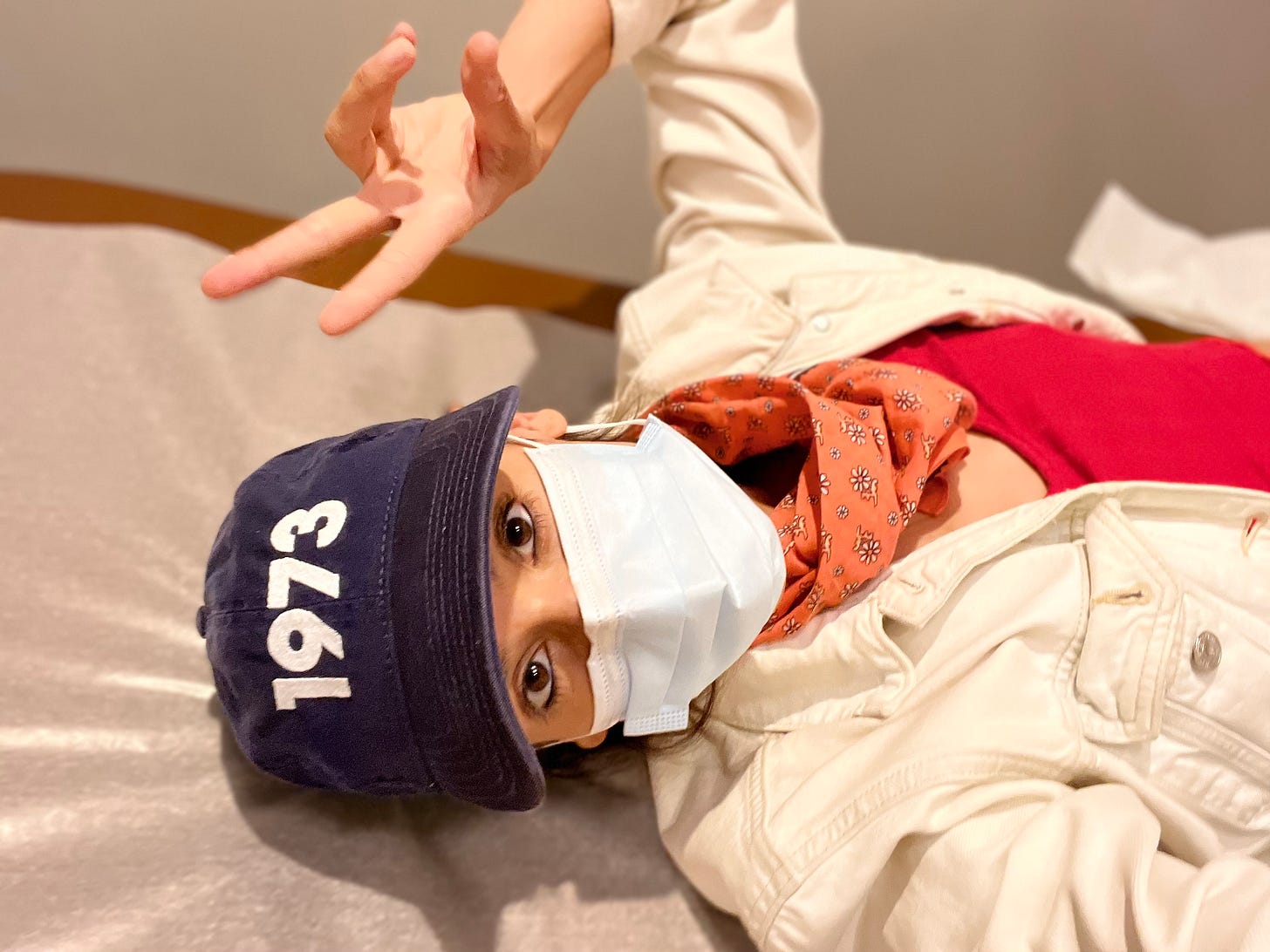 liz wearing a hat that says 1973 with a surgical mask on a doctor table