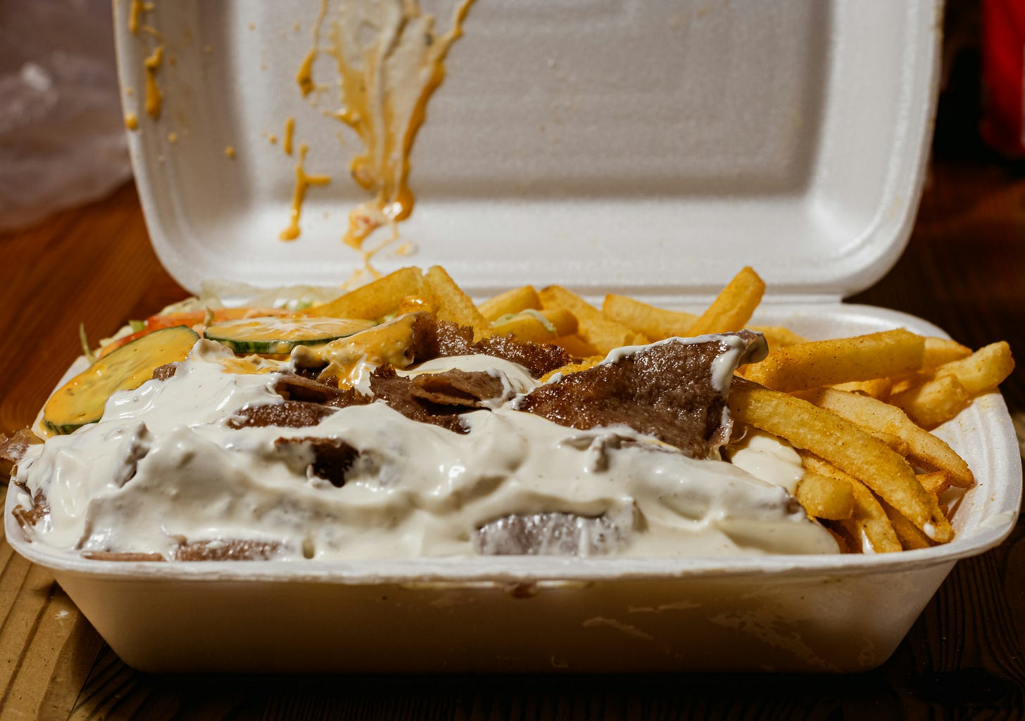 Take-out container with fries and meat, covered in mayonnaise