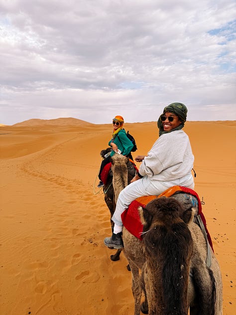 3 photos: 1- Anela holds up a clear embossed glass of tea in one hand, with a gold almost filigree rim. 2-two women ride camels through the desert, looking back smiling. 3-a fire pit glows in the dark in front of a swimming pool and the dark sky above it.