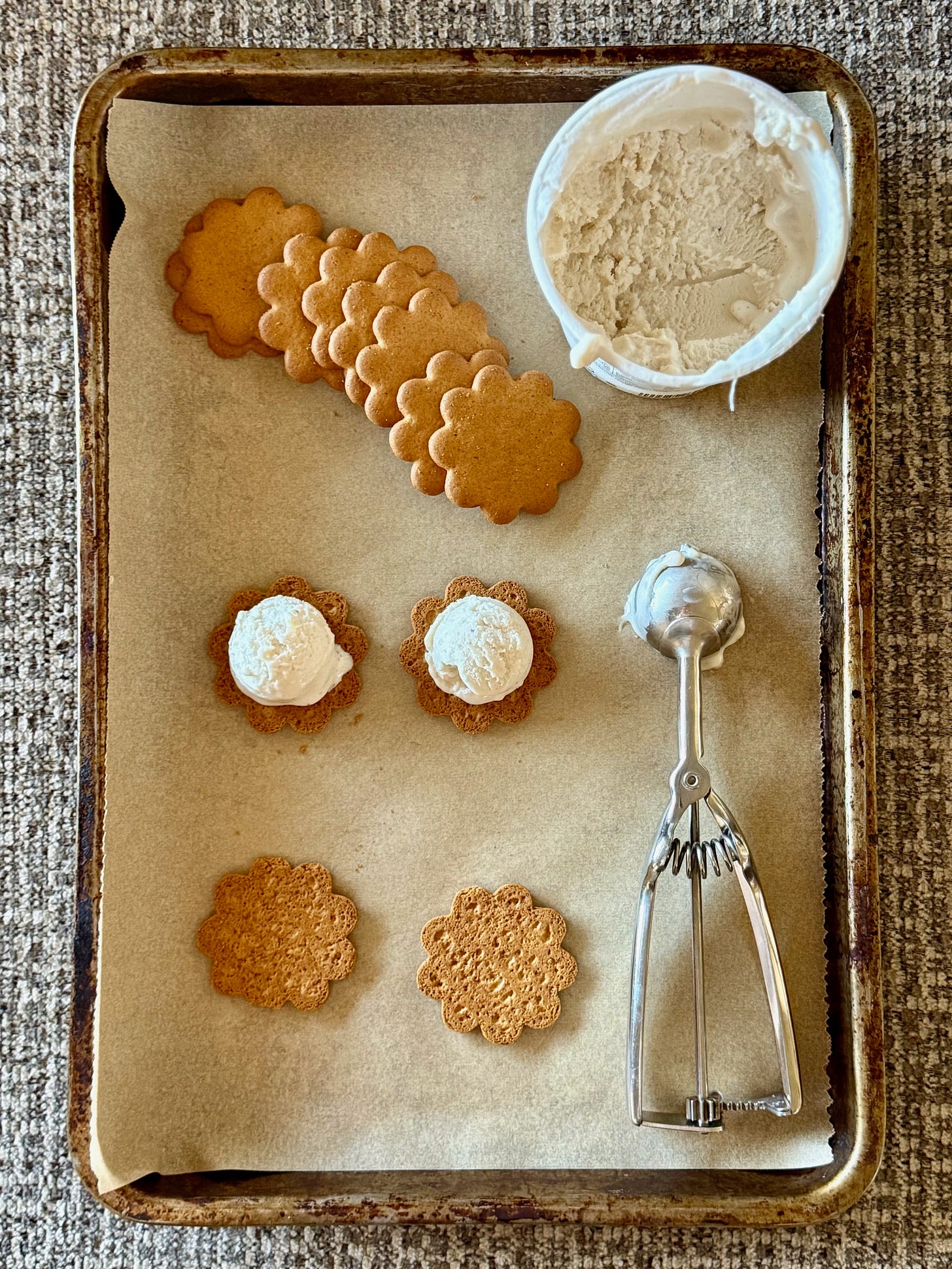A tray with cookies, ice cream and an ice cream scoop, showing process of making mini ice cream sandwiches. 