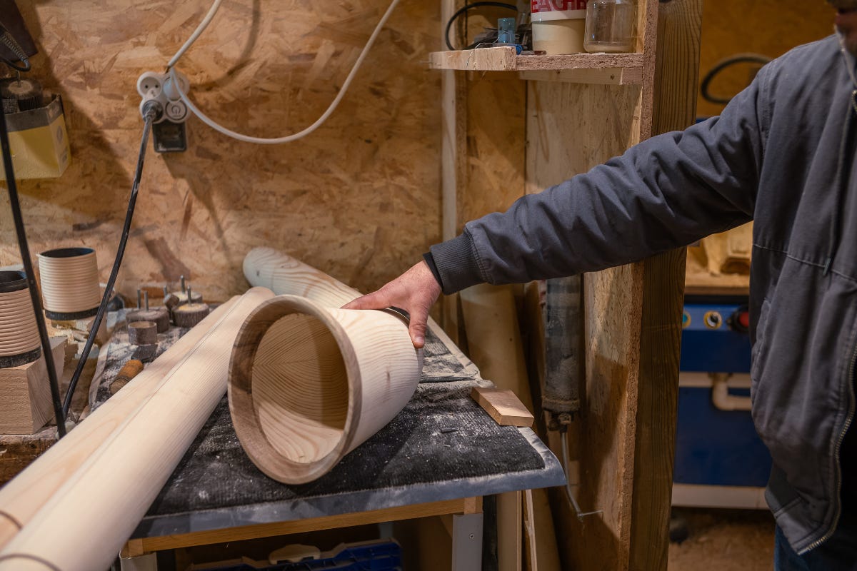 A curved wooden alphorn rests on a work surface with sawdust, showcasing the craftsmanship of its smooth, natural grain.