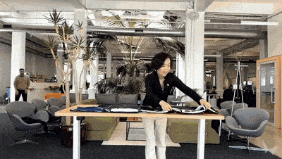 A woman in an open-plan office opens a case and sets up a laptop on a height-adjustable standing desk. A woman in an open-plan office opens a case and sets up a laptop on a height-adjustable standing desk.