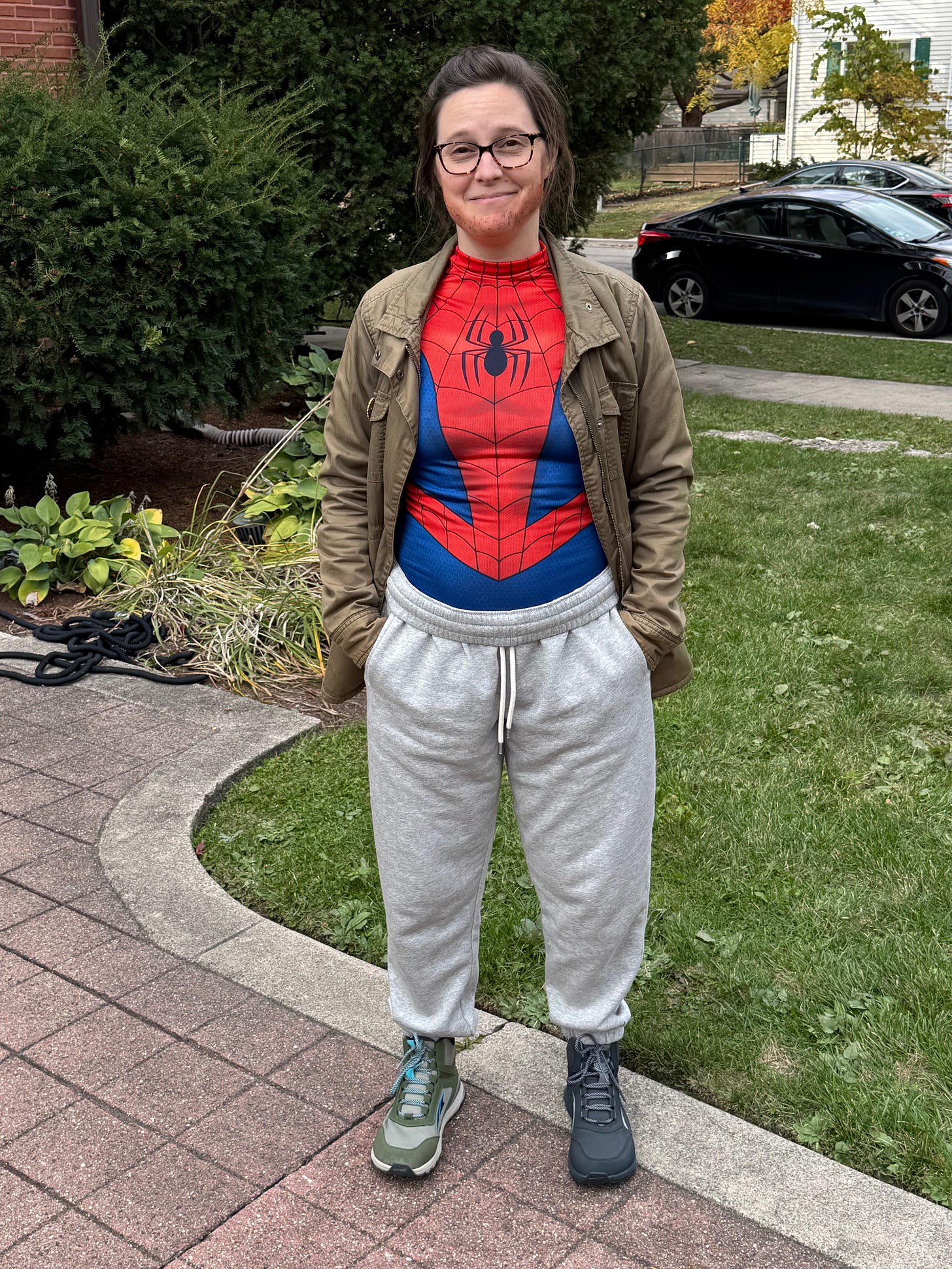 a photo of me dressed as Peter B. Parker. I'm wearing a Spiderman top, sweatpants, an olive green utility jacket, and two mis-matched hiking boots. I have stubble painted on my jaw line.
