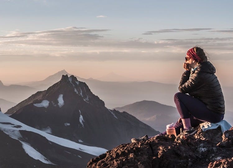 a woman sitting on top of a mountain next to snow covered mountains