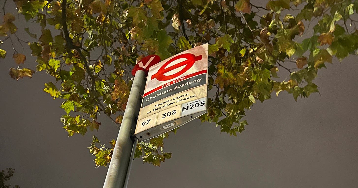 Photo of a bus stop flag sign, timetable and shelter against a night's sky.