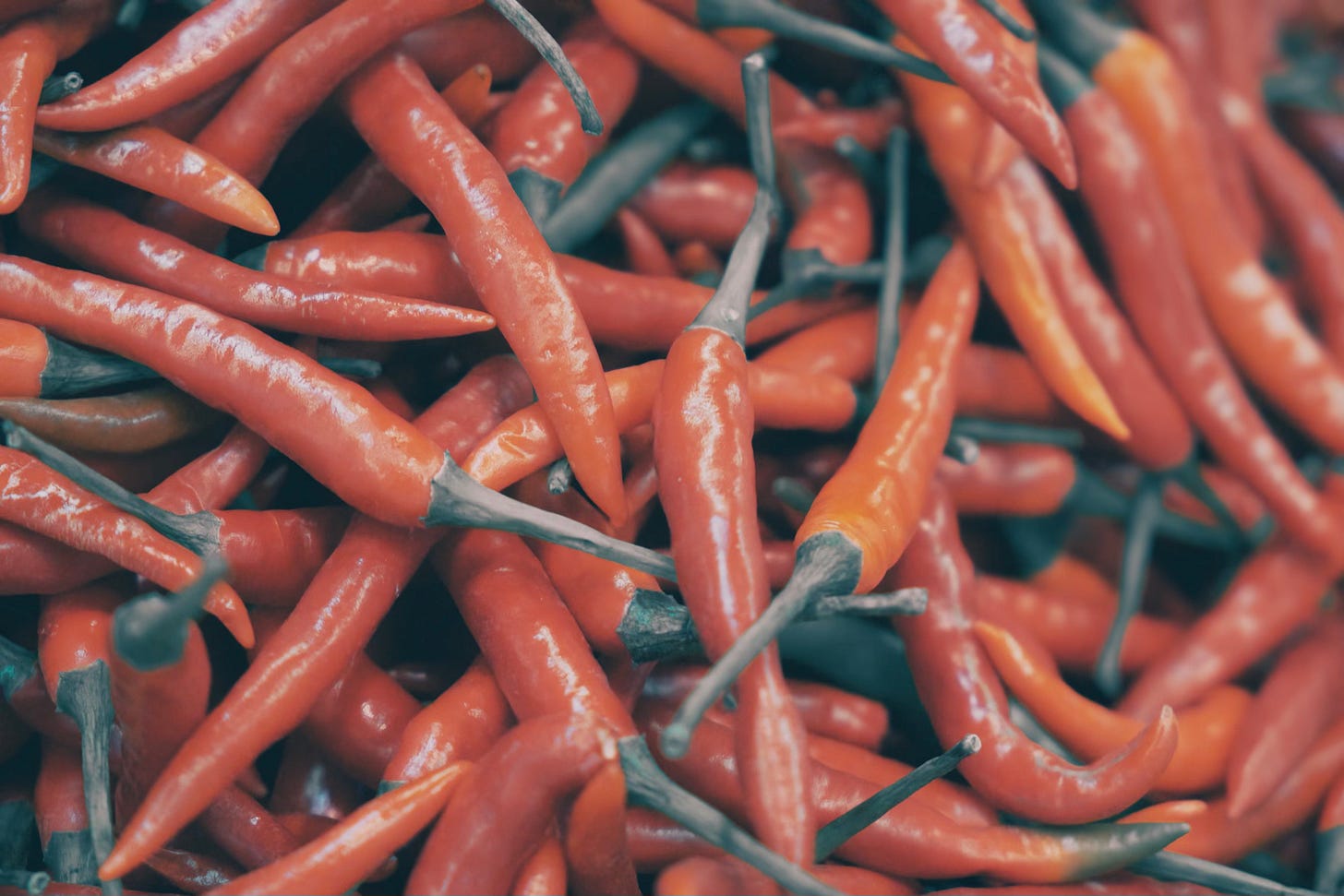Fresh red chili peppers commonly used in spicy food in Switzerland, stacked together with green stems.