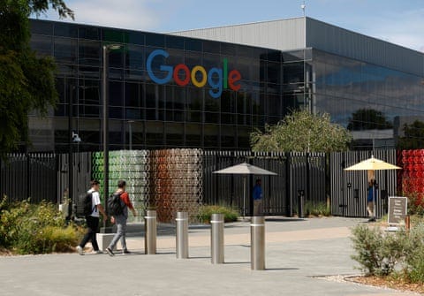 Two people walk past colorful letter sculptures and umbrellas toward a building with the Google logo