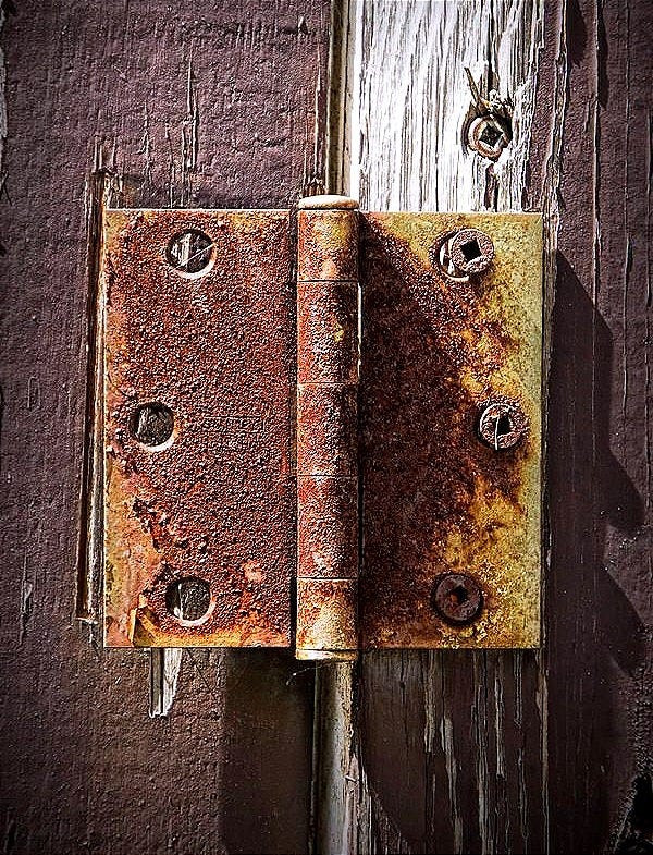 Rusted metal hinge on a weathered wooden door.